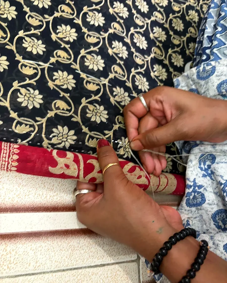 Hands threading a needle over block-printed fabric.
