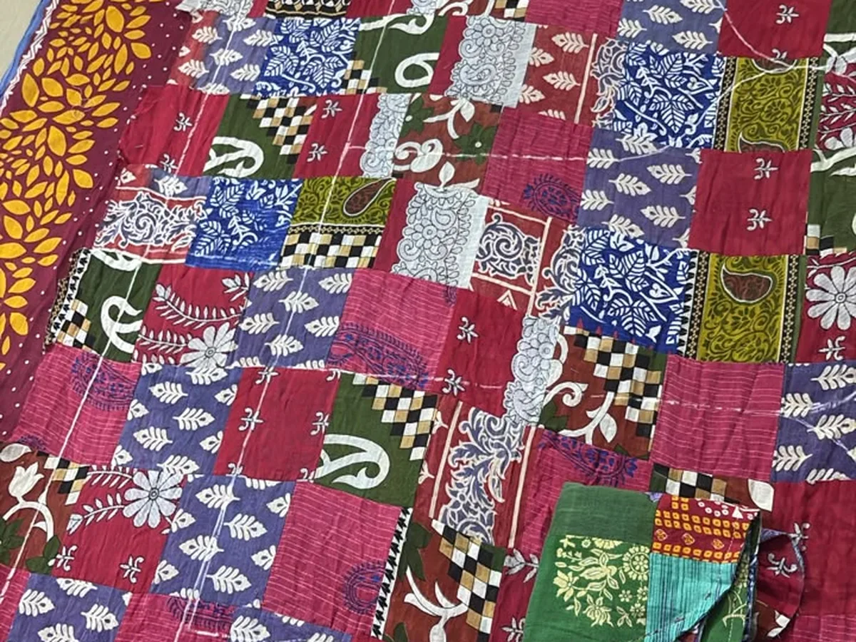 A patchwork quilt stitched from pieces of red, green and white sari fabric.
